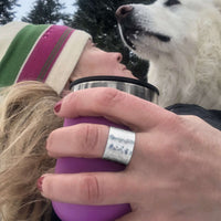 A woman wearing a Rubble Ring, holding a purple cup, with a white dog in a snowy landscape.