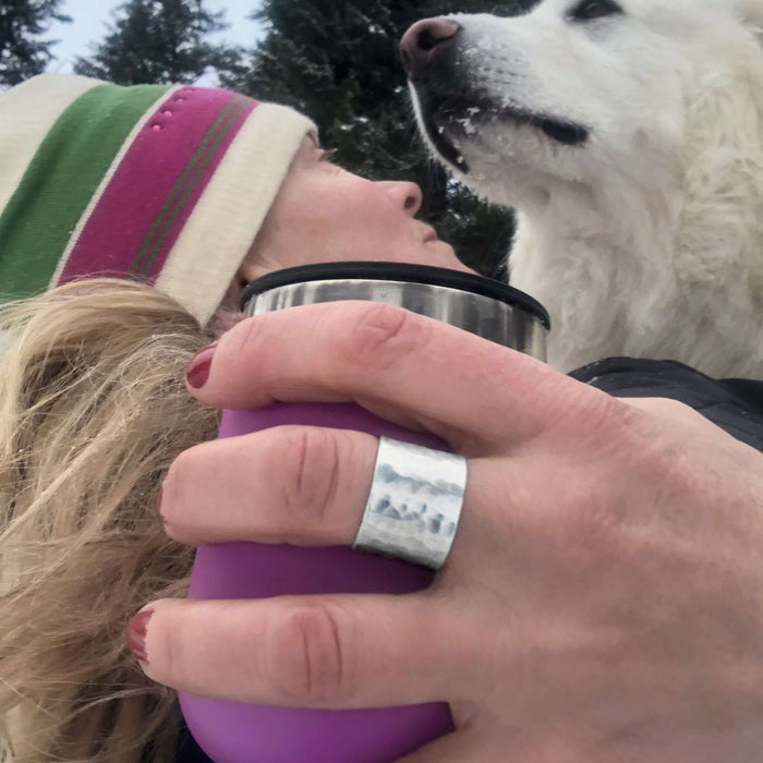 A woman wearing a Rubble Ring, holding a purple cup, with a white dog in a snowy landscape.