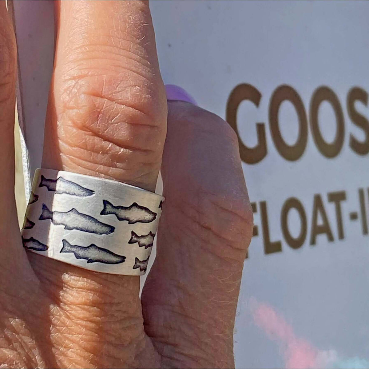 Salmon Run Adjustable Ring displayed on a hand with etched salmon design outdoors
