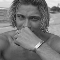 Close-up of a man wearing a Salmon Run Cuff Bracelet at the beach, showcasing its unique design and craftsmanship.