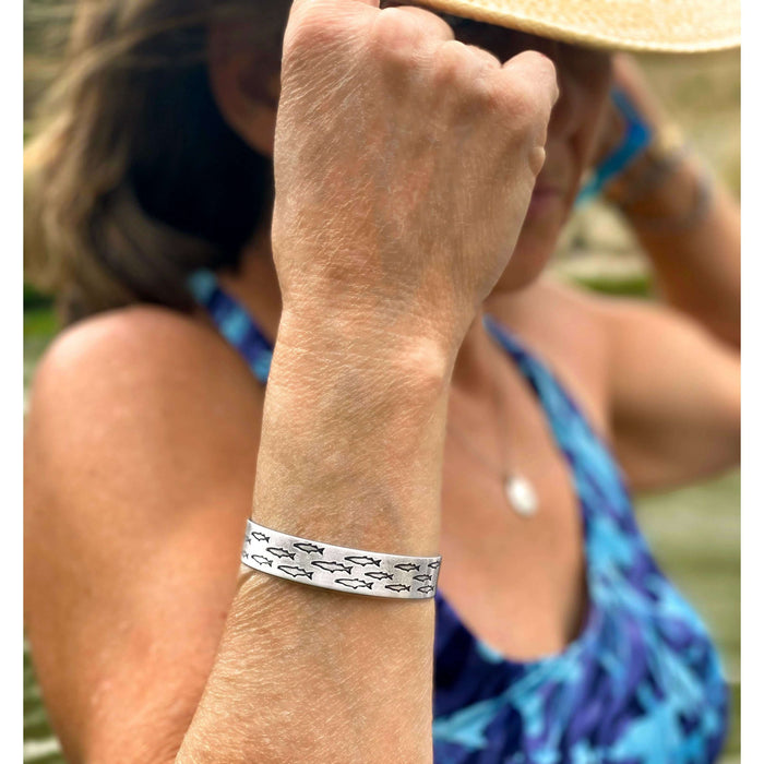 Woman wearing Salmon Run Cuff Bracelet outdoors, showcasing its unique design with fish patterns.