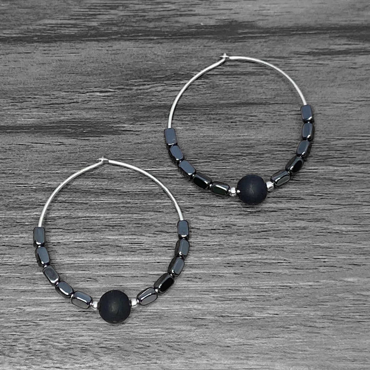 Shun Hematite Beaded Hoop Earrings with shungite and hematite beads on a wooden surface.