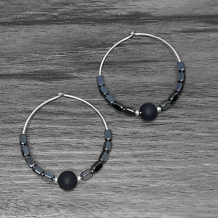 Shun Hematite Beaded Hoop Earrings with shungite and hematite beads on a wooden surface.