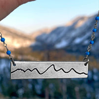 Simple Teton Mountain Necklace showcasing etched brass pendant with Teton mountain range outline.