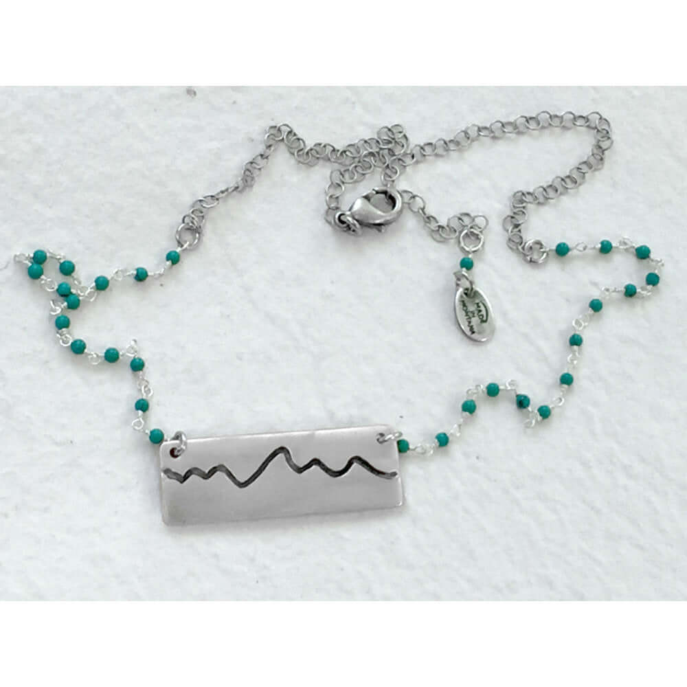 Simple Teton Mountain Necklace featuring a brass pendant and turquoise beaded chain.