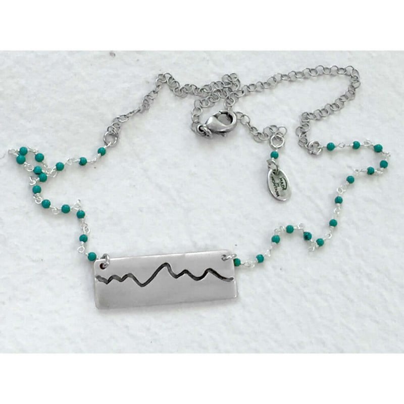 Simple Teton Mountain Necklace featuring a brass pendant and turquoise beaded chain.