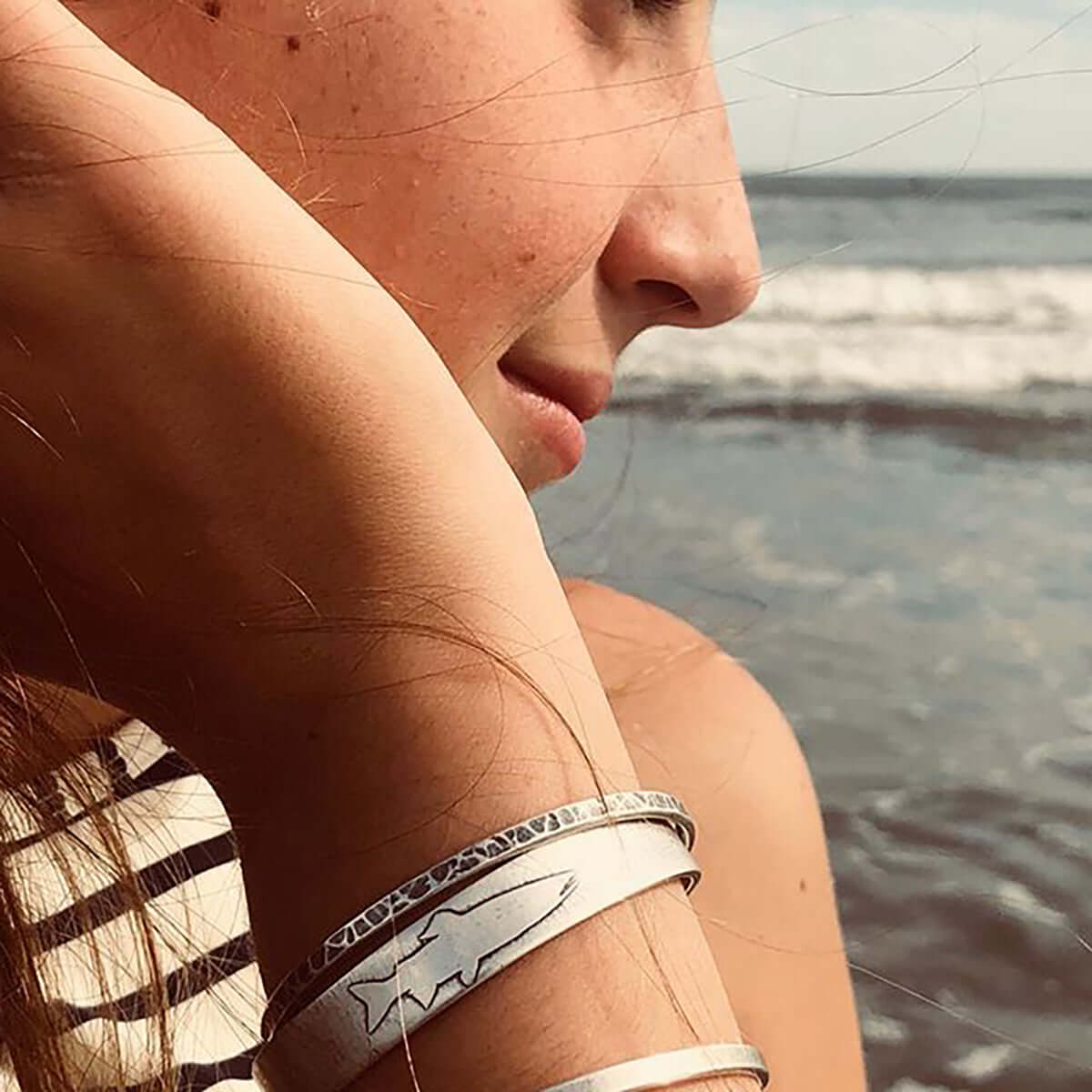 Single Trout Cuff Bracelet worn on a woman's wrist by the beach, highlighting its adjustable design and fishing theme.
