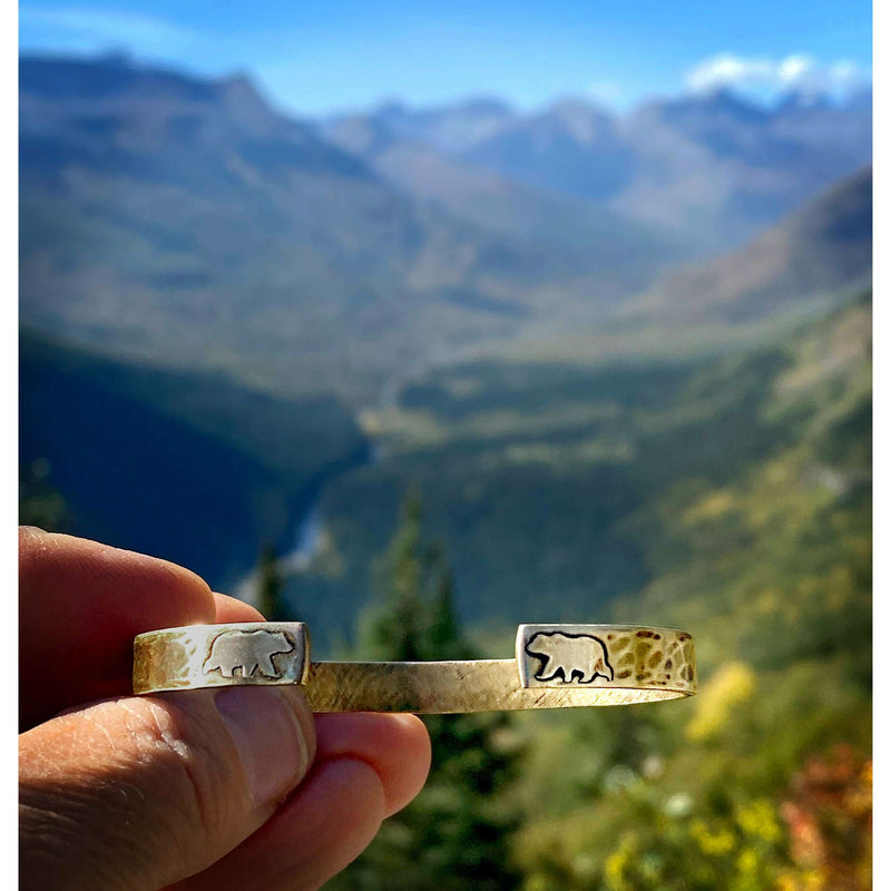 Skinny Bear Cuff Bracelet shown in nature, featuring bear symbols on a textured raw brass cuff.