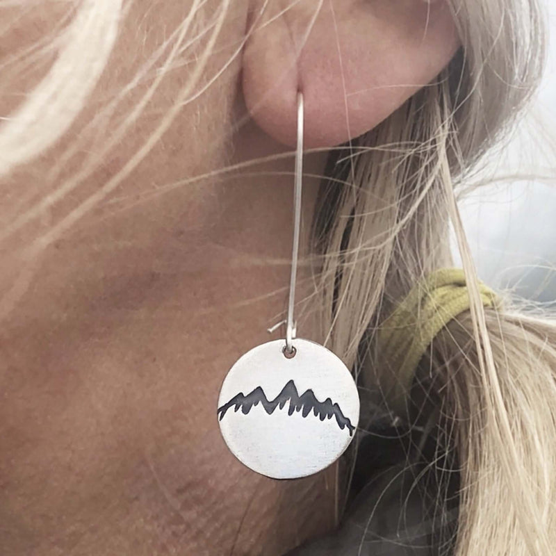 Snowcap Mountain Earrings showcasing snowcapped mountain designs on elegant round disks worn on a model's ear.