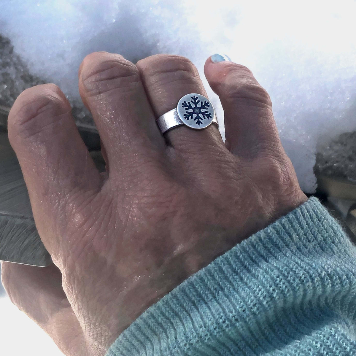 Snowflake Adjustable Ring on a hand, showcasing its charm and winter theme against a snowy background.