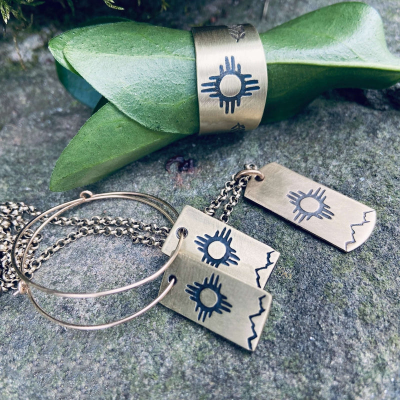 Sol Hoop Earrings displayed with Zia sun design on raw brass, showcasing unique artisan craftsmanship.