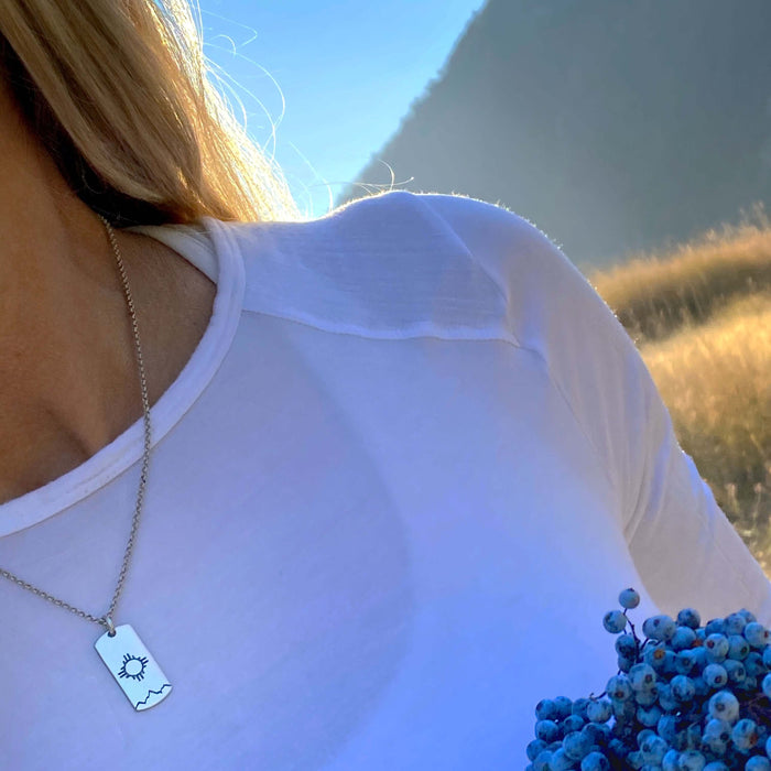 Sol Necklace worn on a woman, showcasing the Zia sun design in a natural outdoor setting.
