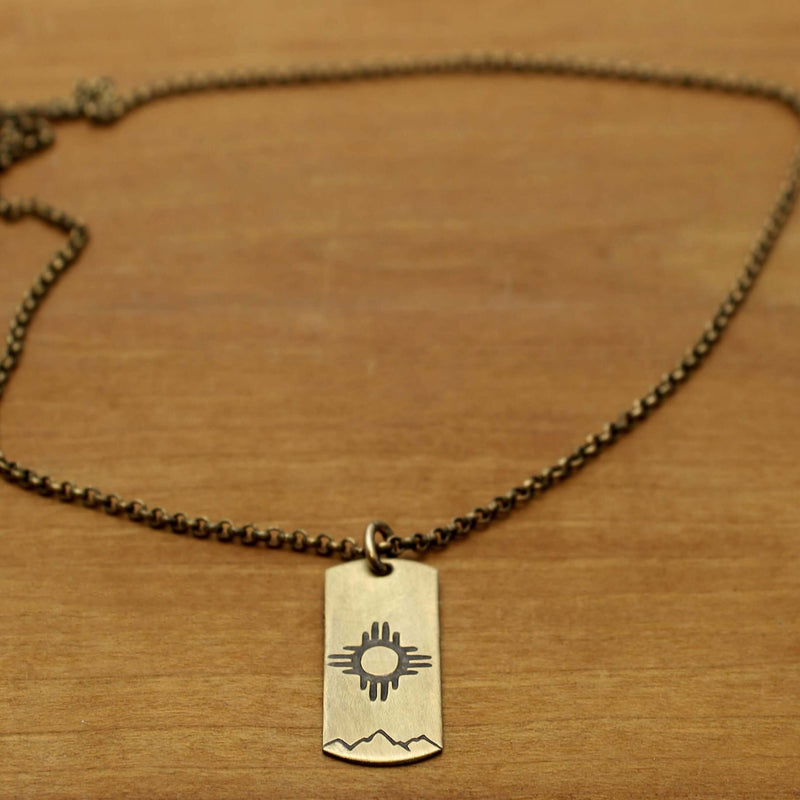 Sol Necklace featuring Zia sun design on raw brass with a chain on wooden background.