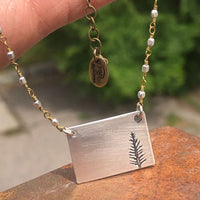 Close-up of the Spruce Necklace featuring a rectangular pendant with a fern design and a beaded chain.
