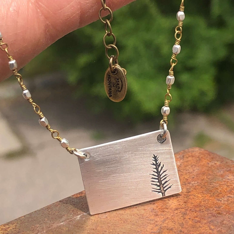 Close-up of the Spruce Necklace featuring a rectangular pendant with a fern design and a beaded chain.