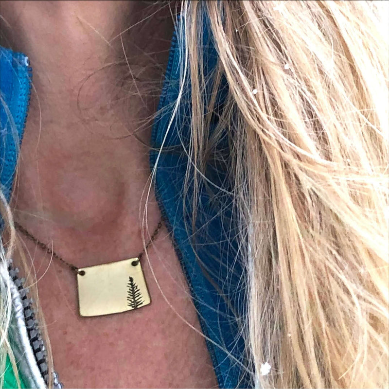 Spruce Necklace worn by a person, showcasing a pendant with a tree design on a chain.