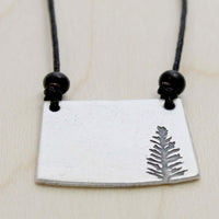 Spruce Necklace featuring a matte silver pendant with a detailed spruce tree design, on an adjustable black cord.