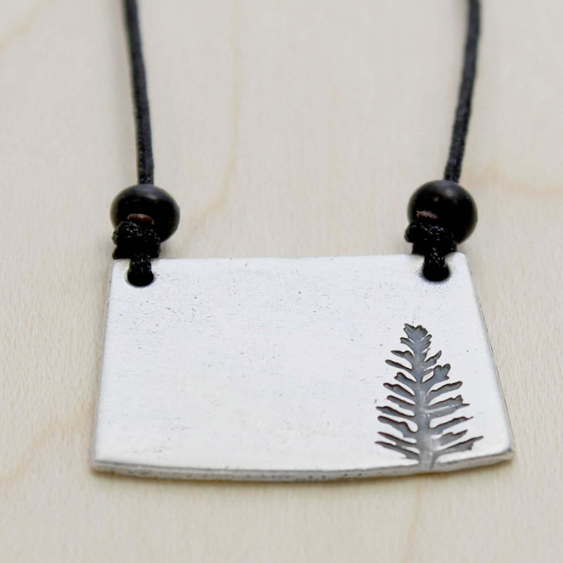 Spruce Necklace featuring a matte silver pendant with a detailed spruce tree design, on an adjustable black cord.