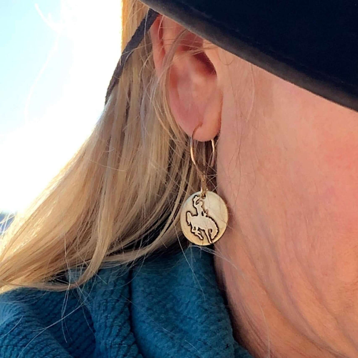 Close-up of a woman wearing Steamboat Earrings depicting a bucking bronco silhouette.