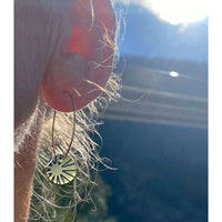 Close-up of Sunrays Earrings hanging from an ear, showcasing the sunlight and design details.