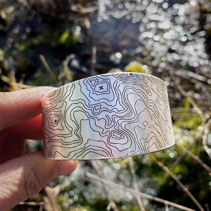 Grand Cuff featuring a unique topographic design, handmade in Montana, adjustable, in matte silver finish.