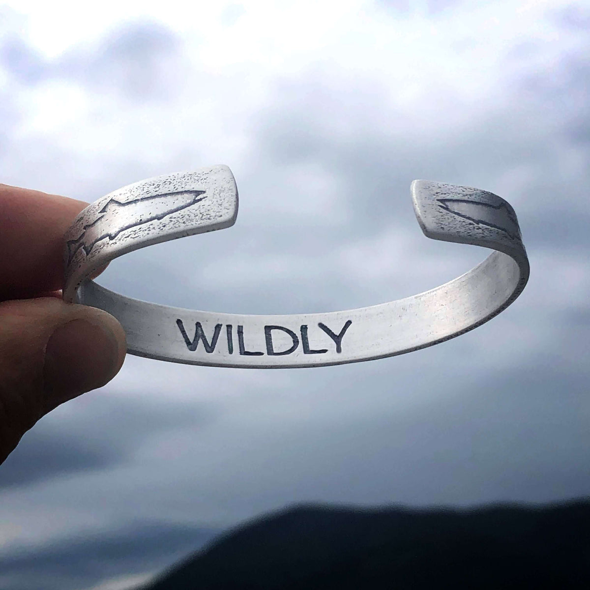 Trout on Tips Cuff Bracelet showcasing the word 'WILDLY' with a natural background.