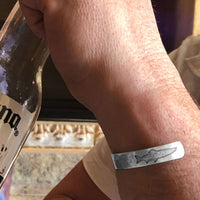 Person wearing Trout on Tips Cuff Bracelet with a drink, showcasing handmade nature-inspired design.