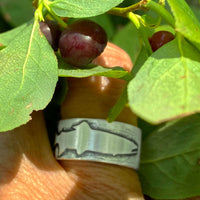 Close-up of handmade Trout Ring featuring etched trout design among foliage and berries.