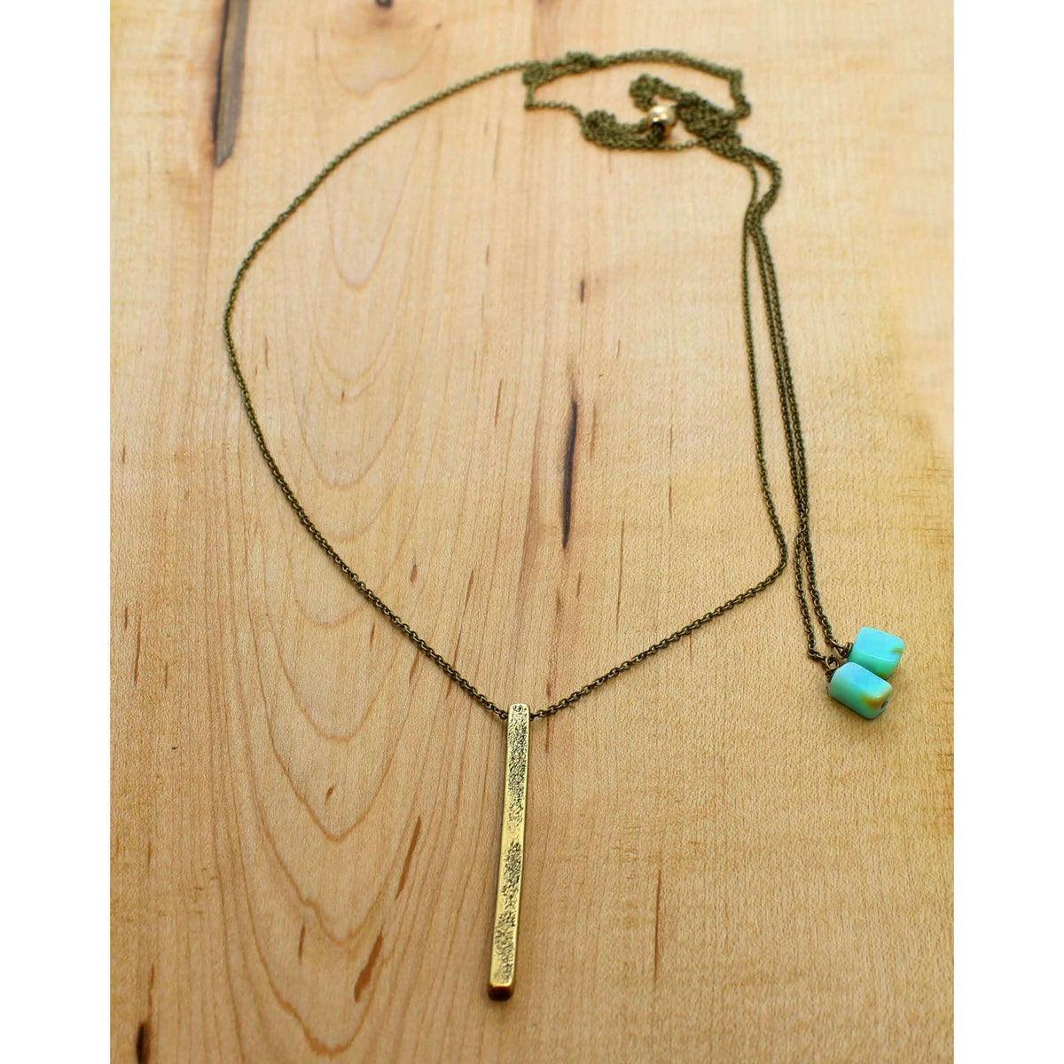 Twig Long Layered Necklace on a wooden surface, featuring a gold twig pendant and teal accents.