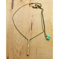 Twig Long Layered Necklace on a wooden surface, featuring a gold twig pendant and teal accents.