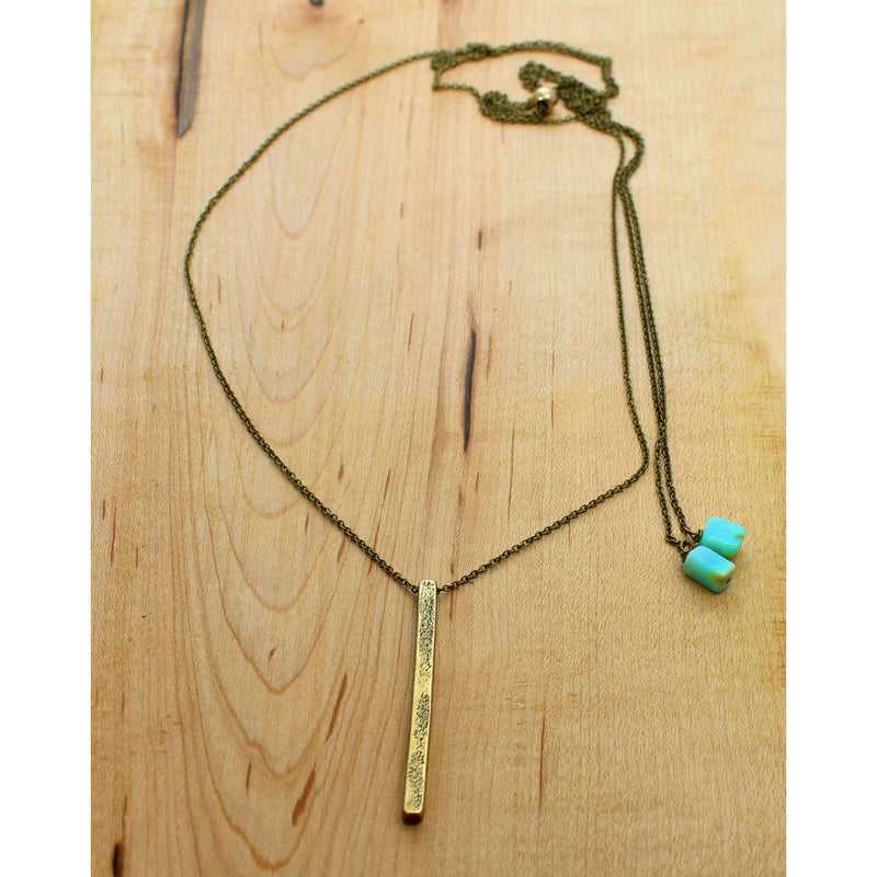 Twig Long Layered Necklace on a wooden surface, featuring a gold twig pendant and teal accents.
