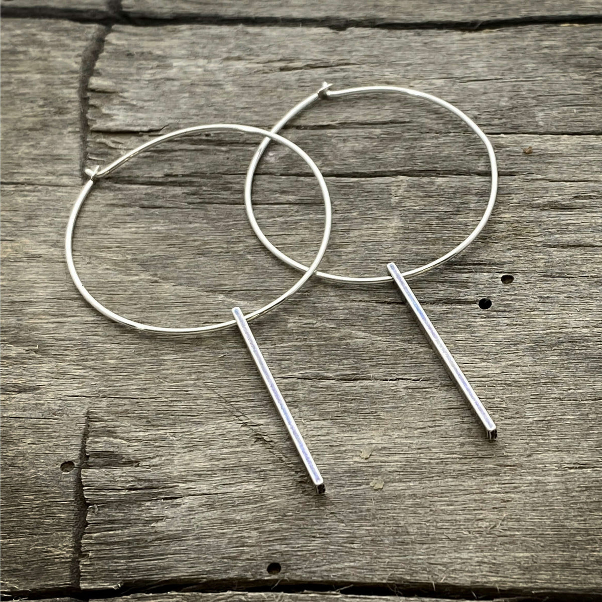 Twigs Hoop Earrings in Matte Silver on a rustic wooden background, showcasing a stylish clean design.