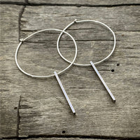 Twigs Hoop Earrings in Matte Silver on a rustic wooden background, showcasing a stylish clean design.