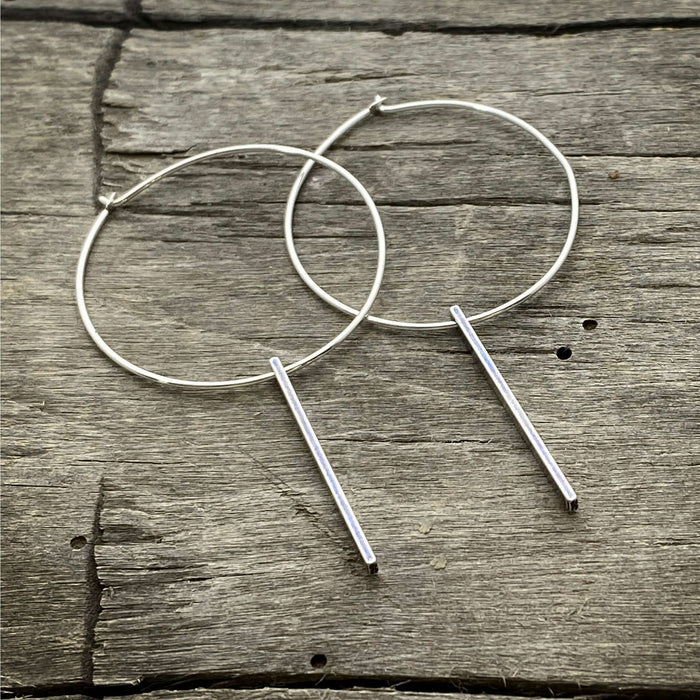 Twigs Hoop Earrings in Matte Silver on a rustic wooden background, showcasing a stylish clean design.
