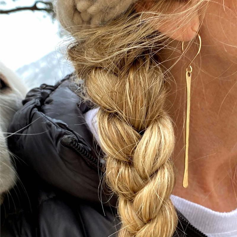 Close-up of a woman wearing Upstream Paddle Earrings, showcasing their elegant design and gold finish.