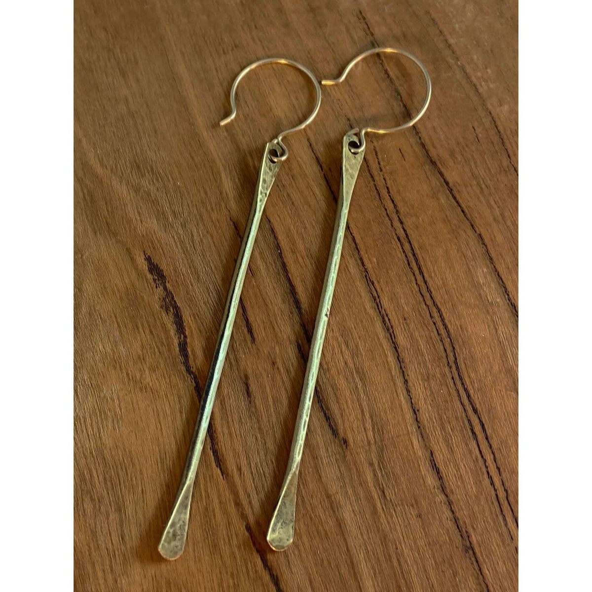 Upstream Paddle  Earrings in brass finish hanging from earwire on wooden background.
