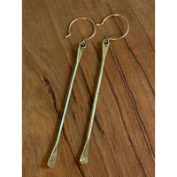 Upstream Paddle  Earrings in brass finish hanging from earwire on wooden background.
