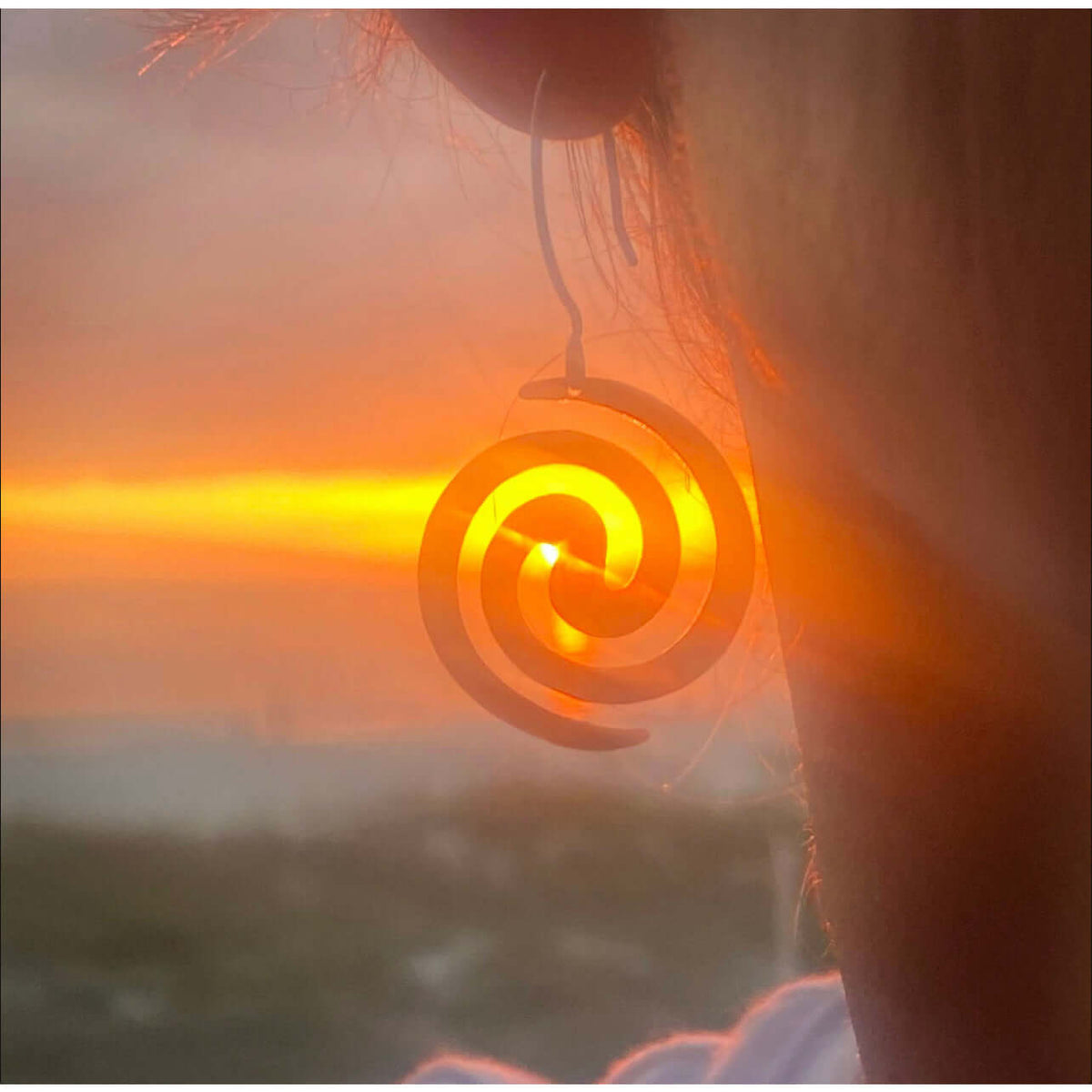Vortex Earrings displayed against a sunset, highlighting their spiral design in matte silver finish.