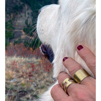 A close-up of a hand wearing Wide Open Adjustable Ring, gently touching a fluffy dog in a natural setting.