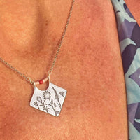 Wildflower Box Necklace showcasing intricate floral designs and stylish pink stones on a silver chain.